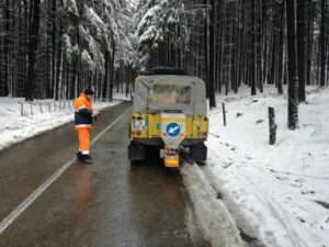 Auto gialla per Protezione Civile con sparginale e uomo vestito in tuta gialla su strada innevata in mezzo al bosco