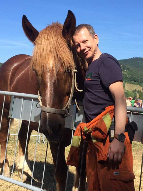 contattaci Uomo vestito con tuta arancione protezione civile e maglietta blu accanto a cavallo