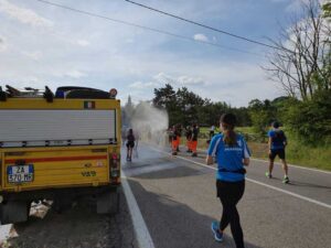 Auto gialla e Uomini in tuta arancione e blu Protezione Civile che bagnano corridori