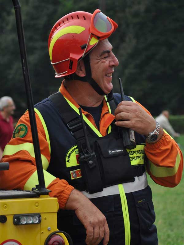 contattaci Uomo vestito con tuta arancione Persona con tuta arancione appoggiata su auto gialla Protezione Civile, casco rosso e gilet nero